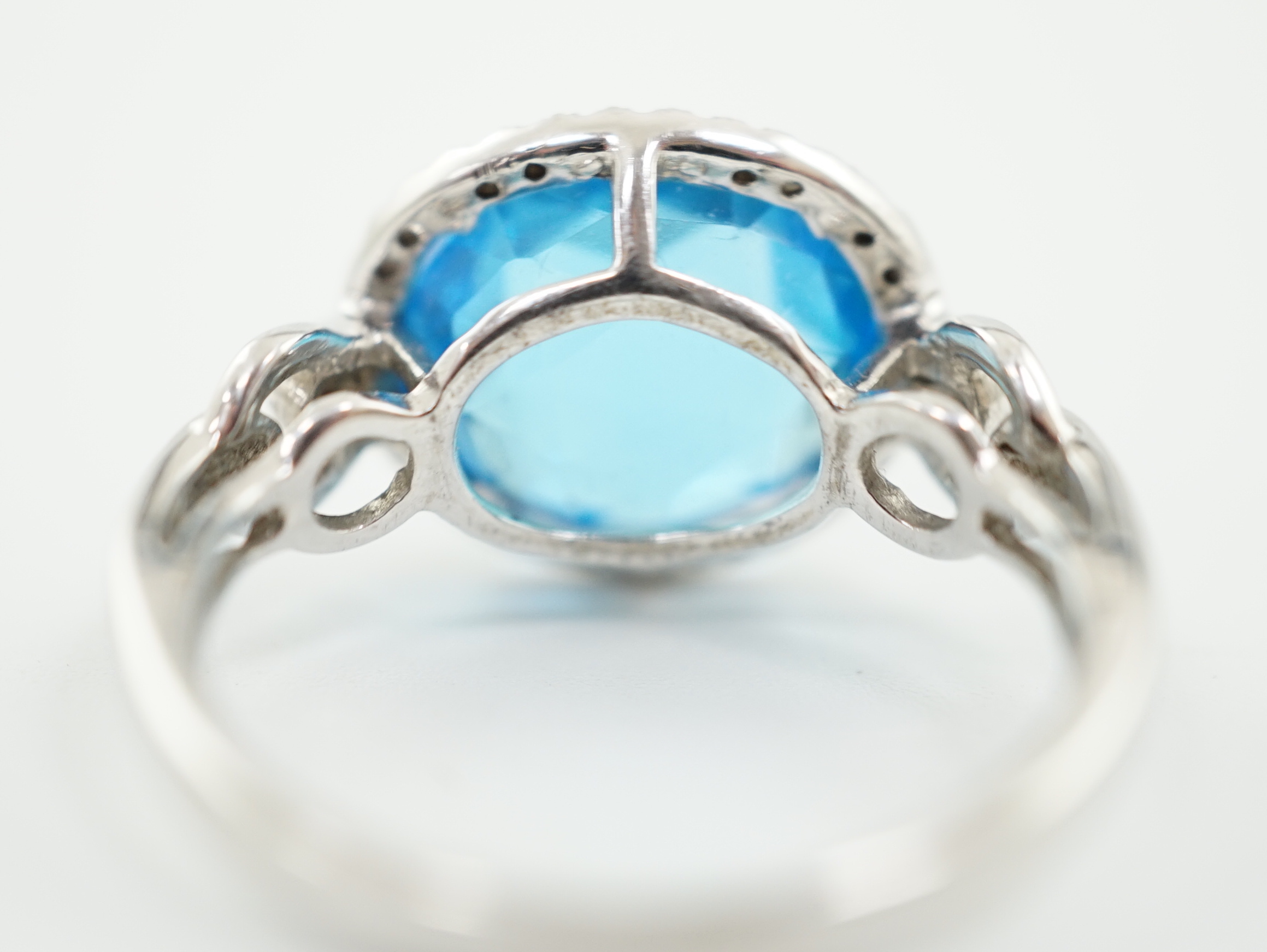 A modern 18ct white gold and facetted oval cut blue topaz set dress ring, with diamond chip set border and shoulders